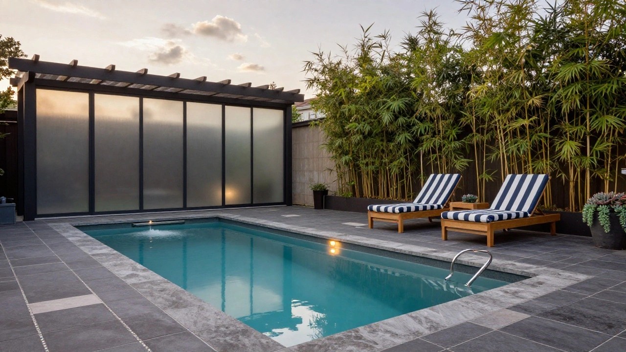 Two wooden lounge chairs with blue-and-white striped cushions on a gray stone deck beside a turquoise pool, screened by tall green bamboo plants next to a frosted glass pavilion.