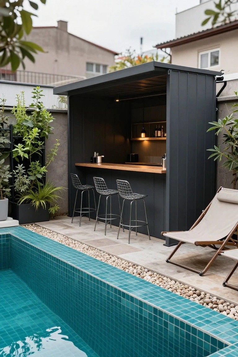 Black outdoor bar pavilion with wooden countertop, metal stools, and shelving next to a turquoise mosaic-tiled inground pool edged in pebbles and plants.