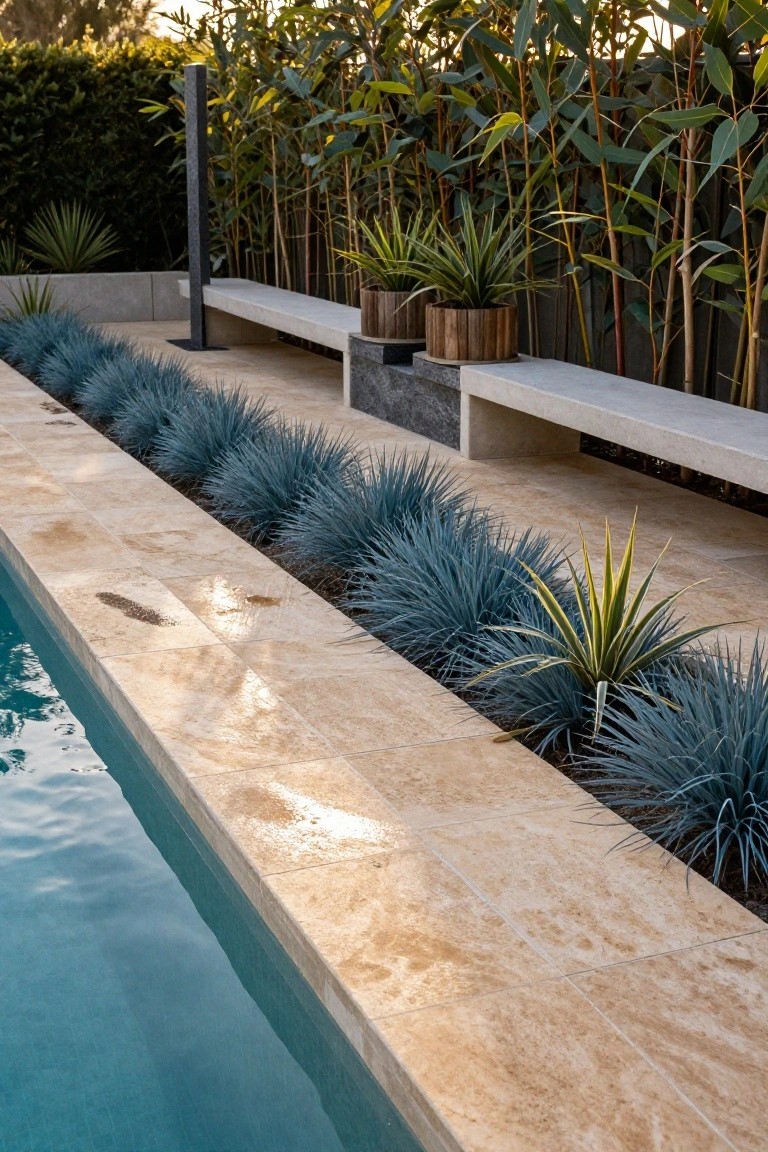 Pool edge with beige travertine tiles lined by massed blue agave plants, nearby yucca, potted plants in wooden tubs, concrete benches, and bamboo screen in the background.