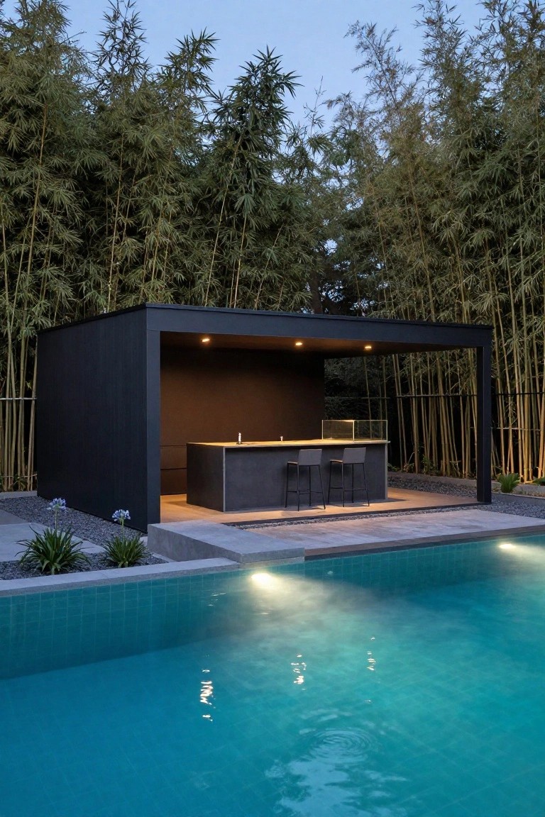 19 Modern Backyard Inground Pool Ideas For Fresh Outdoor Appeal Black rectangular pavilion structure with concrete bar counter, two stools, and overhead lighting next to a turquoise inground pool, surrounded by bamboo plants and gravel ground cover at dusk.