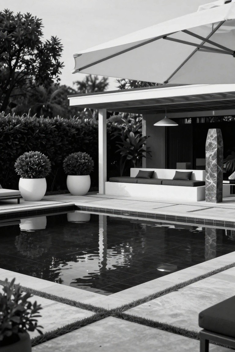 Black-and-white photo of a modern semi-inground pool with dark tiles, adjacent low built-in white bench with black cushions under a covered structure flanked by potted plants and a tall marble pillar.