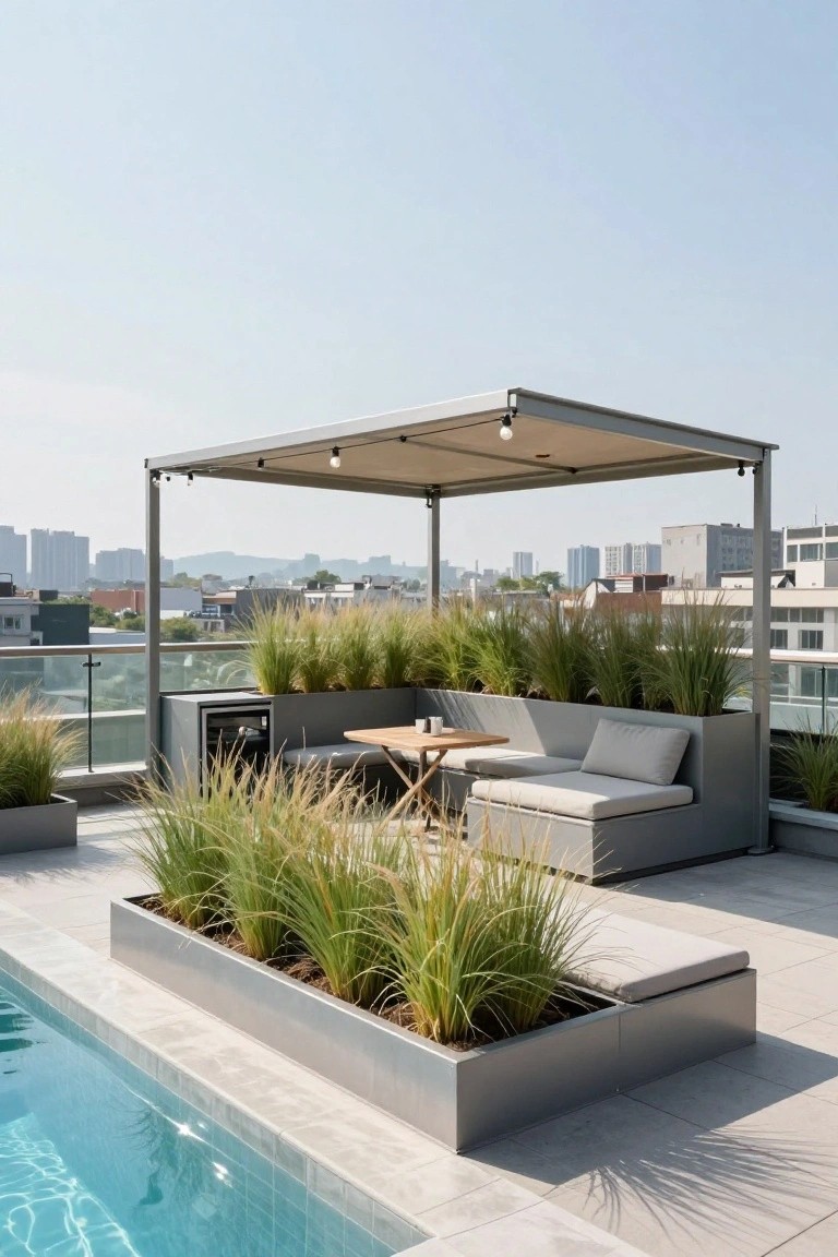 Rooftop terrace with a small rectangular pool next to an L-shaped built-in bench integrated with rectangular planters containing tall ornamental grasses, under a beige fabric-covered metal pergola with string lights, city buildings in the background.
