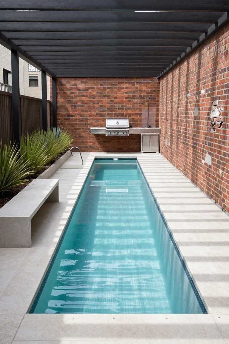 Long narrow in-ground pool with turquoise water in a brick-walled backyard under a black timber pergola, with built-in BBQ kitchen, concrete bench, and agave plants along one side.
