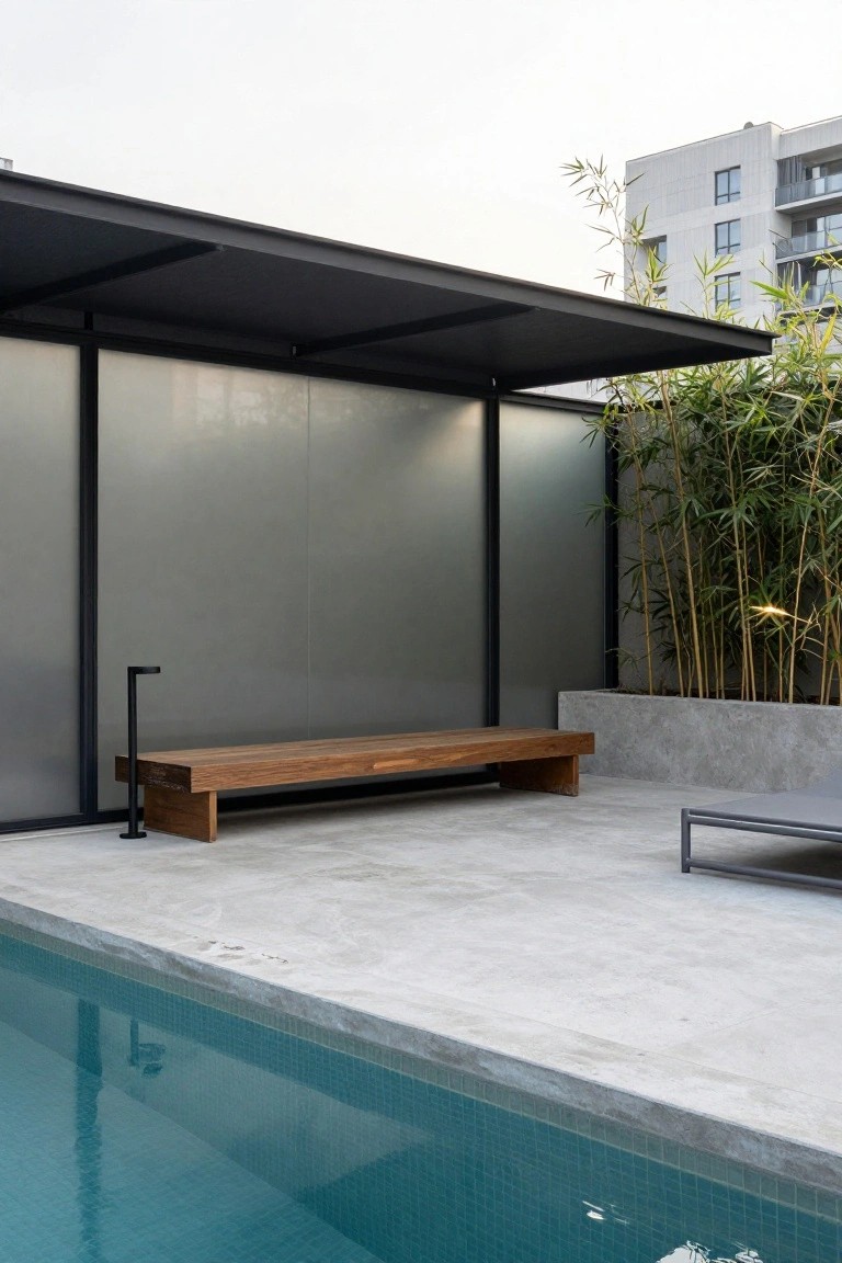 Modern poolside patio with wooden bench, concrete walls, and bamboo plants.