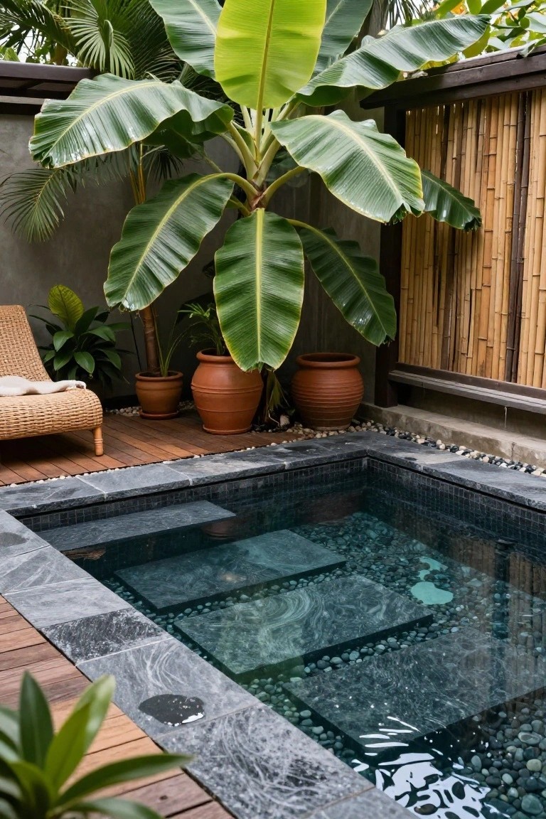 21 Creative Stock Pond Pool Ideas For Nature Loving Yards Small rectangular plunge pool with dark mosaic tiles, pebble flooring, and stone steps, surrounded by lush tropical plants including banana trees, potted greenery, a rattan lounge chair on wooden decking, and bamboo fencing in an outdoor courtyard.