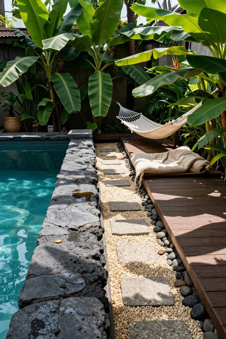 Turquoise pool edged by rugged black stone wall, with pebble-filled stepping stone path leading to wooden deck, tropical plants, and white hammock nearby.