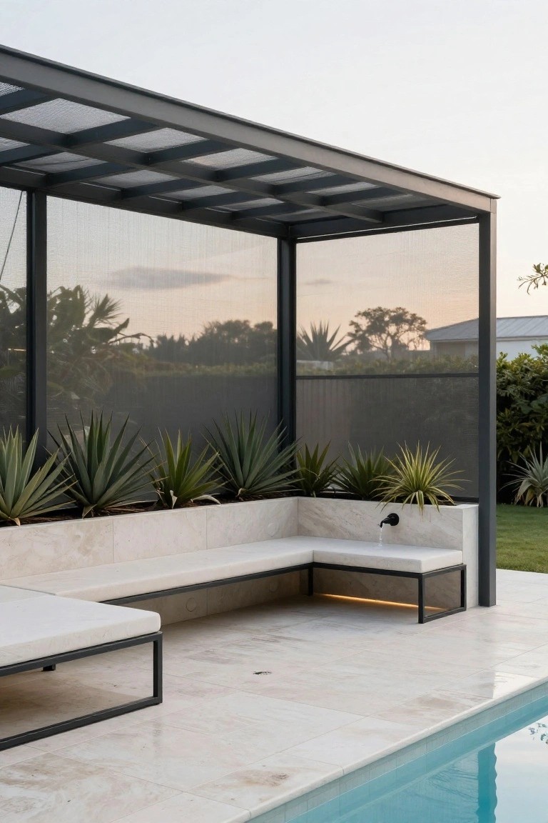 Black metal pergola with mesh side screens and slatted roof shelters an L-shaped white stone bench and low lounger next to a white-tiled pool edge, with potted agave plants along the bench.