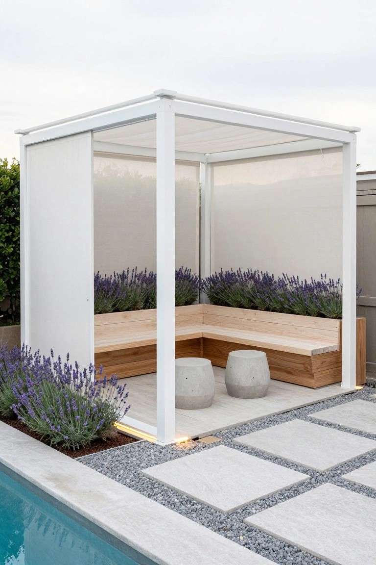 A white open-frame pergola with fabric shades and sliding panels sheltering L-shaped light wood benches integrated with lavender planters on a pebble and light stone paver patio next to an inground pool.