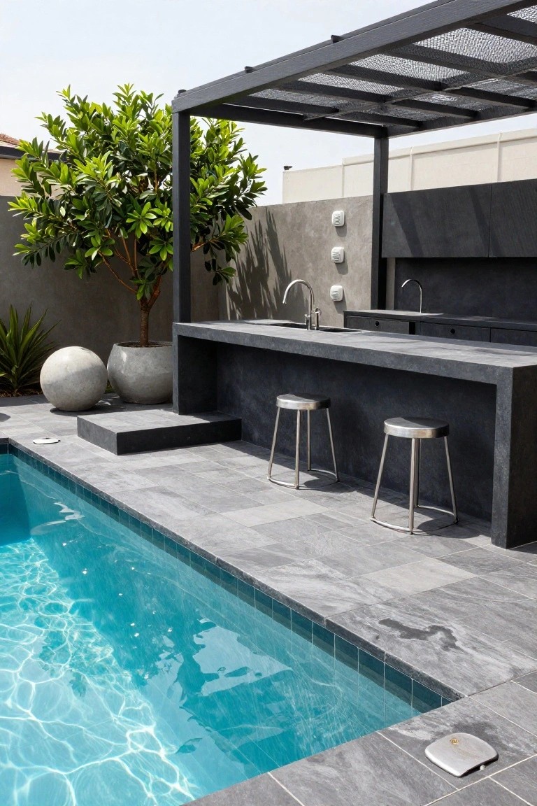 Modern outdoor pool area with a sleek black stone bar counter, sink, two metal bar stools, potted plants, and a metal pergola next to a rectangular inground pool edged in gray tiles.