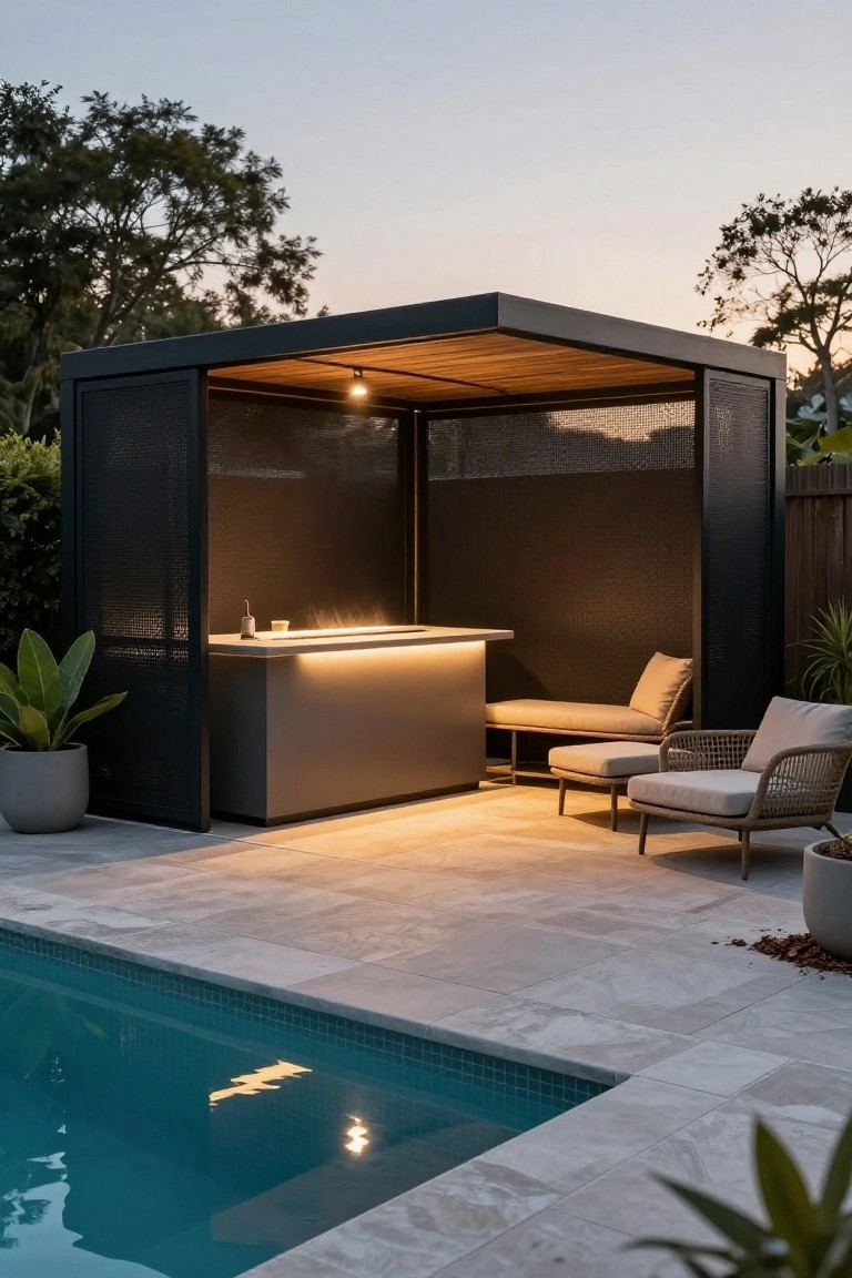 Modern black metal pavilion cabana with mesh side screens and wooden slat roof beside an in-ground pool, featuring a backlit bar counter, cushioned bench and lounge chairs, potted plants, and light gray tiled patio at dusk.