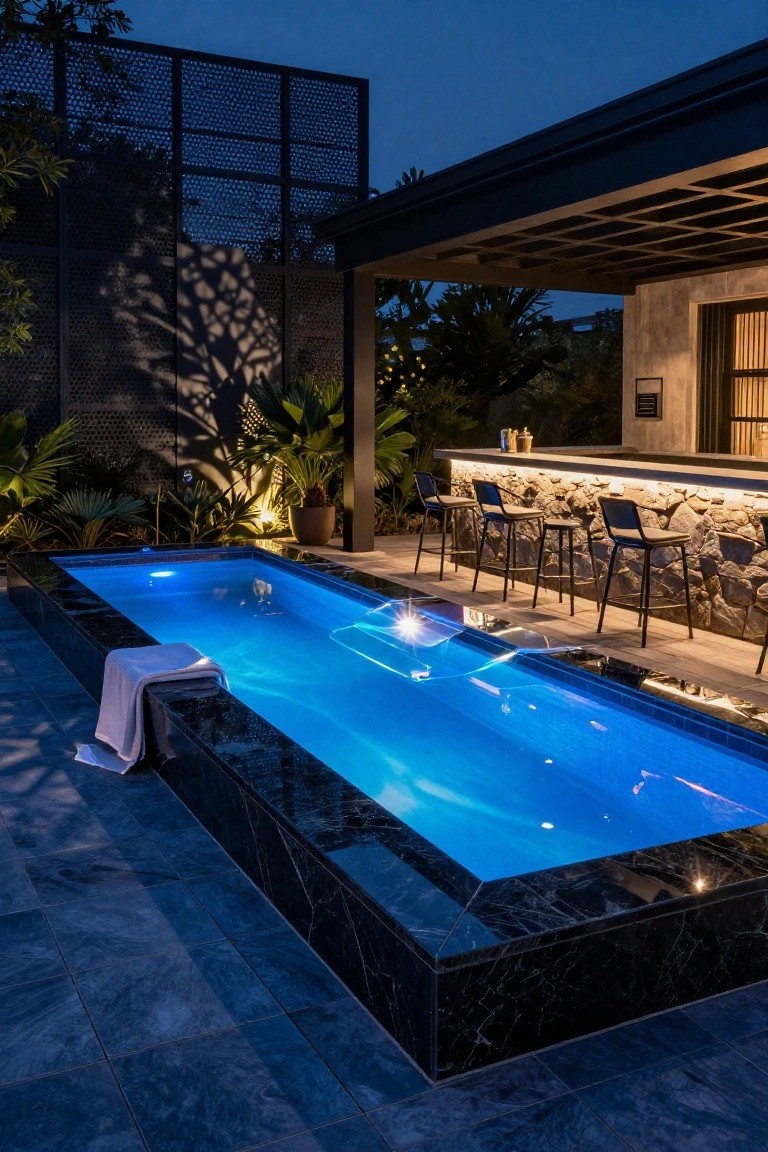 25 Dramatic Dark Blue Pool Tile Ideas With Visual Depth Rectangular pool with dark blue water and black marble edges at night, adjacent to a stone bar with four stools, surrounded by tropical plants and dark tiled decking.
