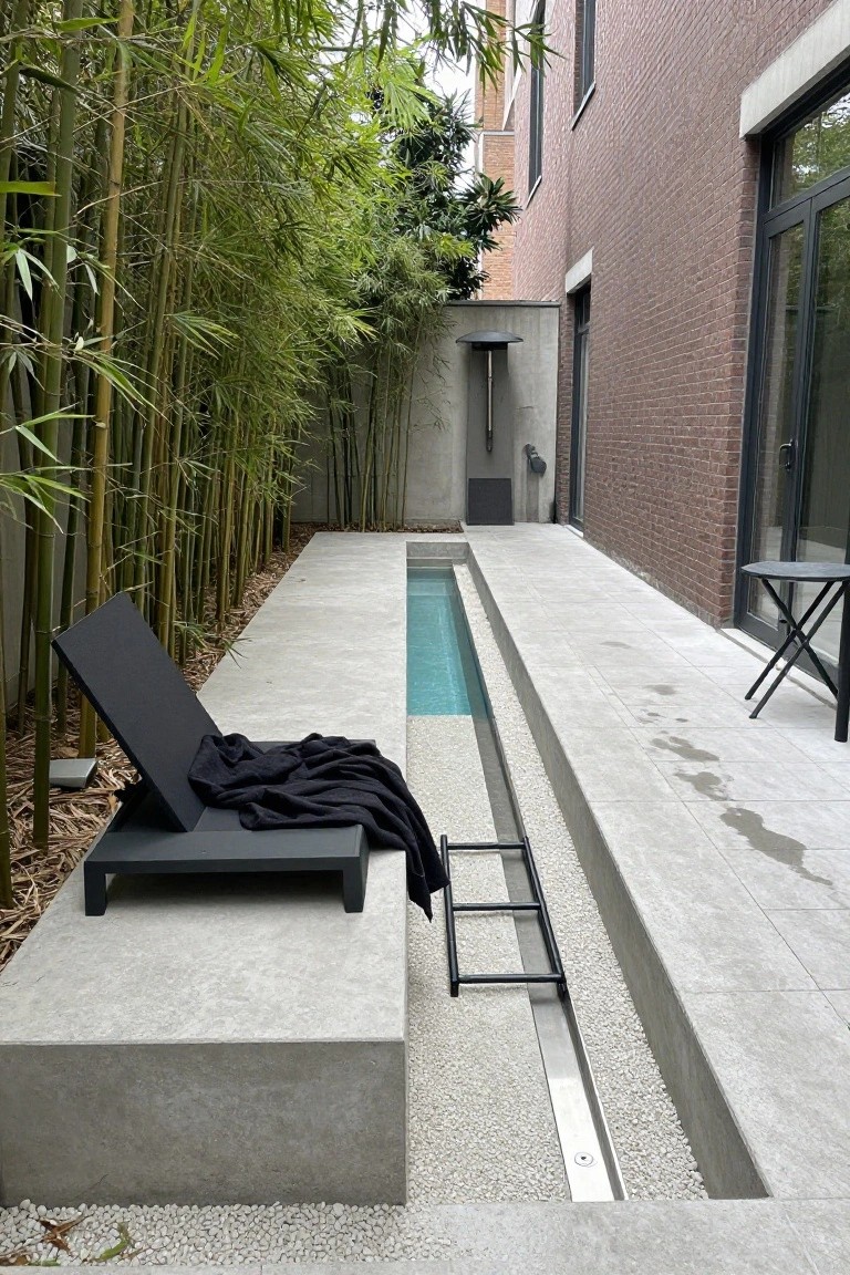 25 Upgraded Stock Tank Pool Ideas For A Big Style Boost Narrow turquoise lap pool set into concrete decking alongside a brick wall, screened by bamboo plants, with a black lounge chair draped in a towel, small black table, and metal ladder nearby.