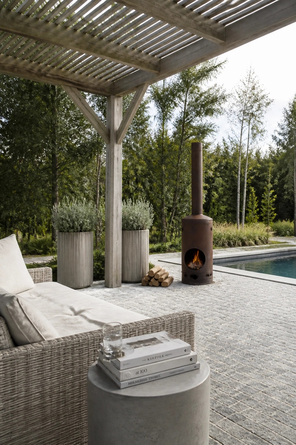 Outdoor patio with wicker sofa, fireplace, pool, potted plants under wooden pergola