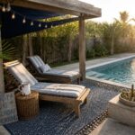 Wooden lounge chairs sit on patterned rugs beneath a pergola covered by a black fabric shade next to a rectangular swimming pool.