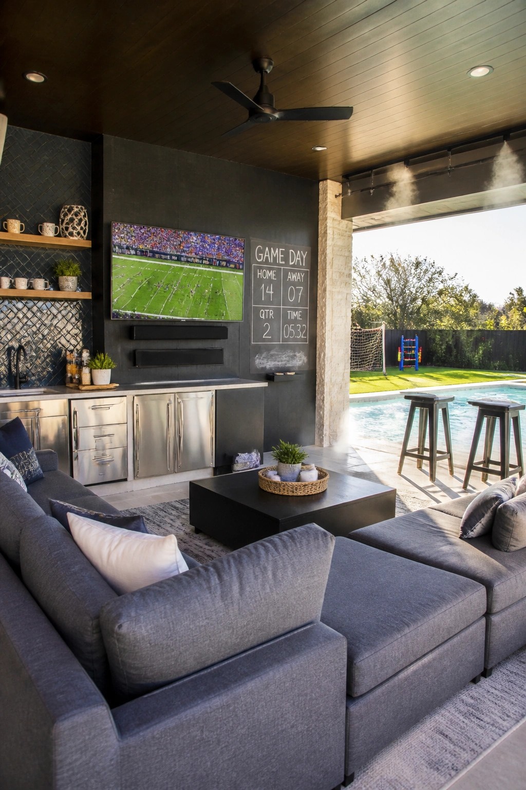 Modern outdoor patio with gray sectional sofa, TV showing football, and pool view