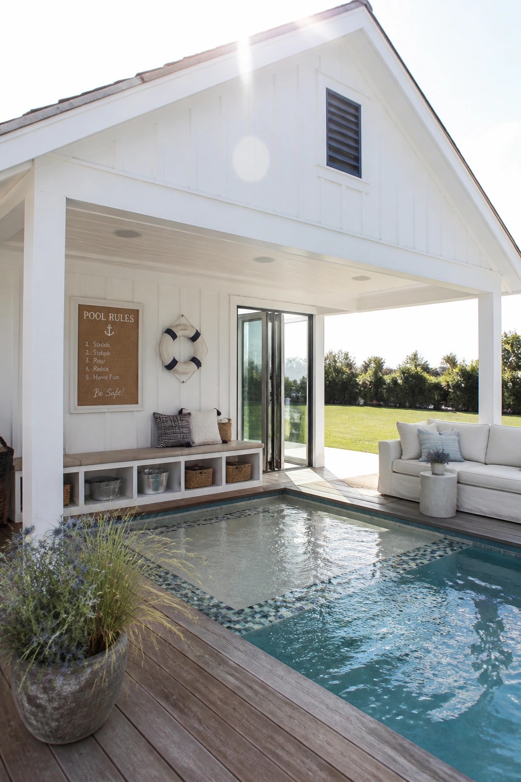 A white covered pool pavilion with built-in bench storage, a pool rules sign, and an adjacent swimming pool on a wooden deck.