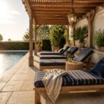 Wooden lounge chairs with blue striped cushions arranged under a pergola next to a swimming pool.