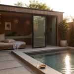 Modern wooden pool house with bed beside pebble-lined swimming pool and potted plants