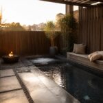 A narrow rectangular pool with a fire pit on gravel to the left and a long wooden bench with cushions along the right side, plus a bubbling spa section at the far end.