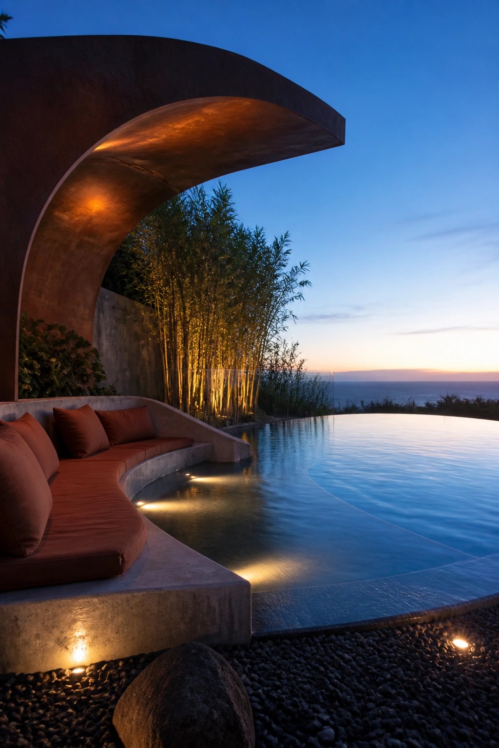 A curved concrete shade canopy with built-in bench seating next to an infinity pool at dusk.