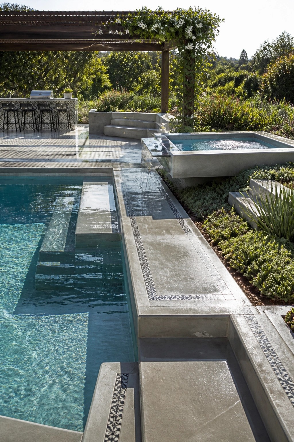 A rectangular swimming pool with submerged concrete platforms and a long concrete water channel that spills from a raised basin along the pool edge.