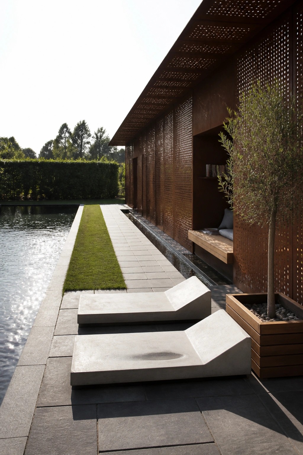 22 Contemporary Pool Shade Ideas in Minimalist Outdoor Settings A minimalist outdoor pool area with two concrete lounge chairs on dark stone paving, a narrow lawn strip, a long rectangular pool, and a rusted metal building with perforated panels and a built-in bench.