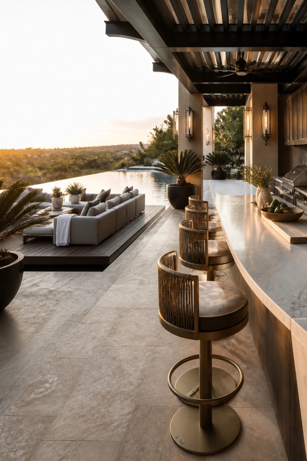 23 Fresh Pool Patio Furniture Ideas That Create Comfortable Outdoor Gathering Spaces An outdoor patio with a long marble bar counter, four metal bar stools, lounge seating, and a swimming pool in the background.