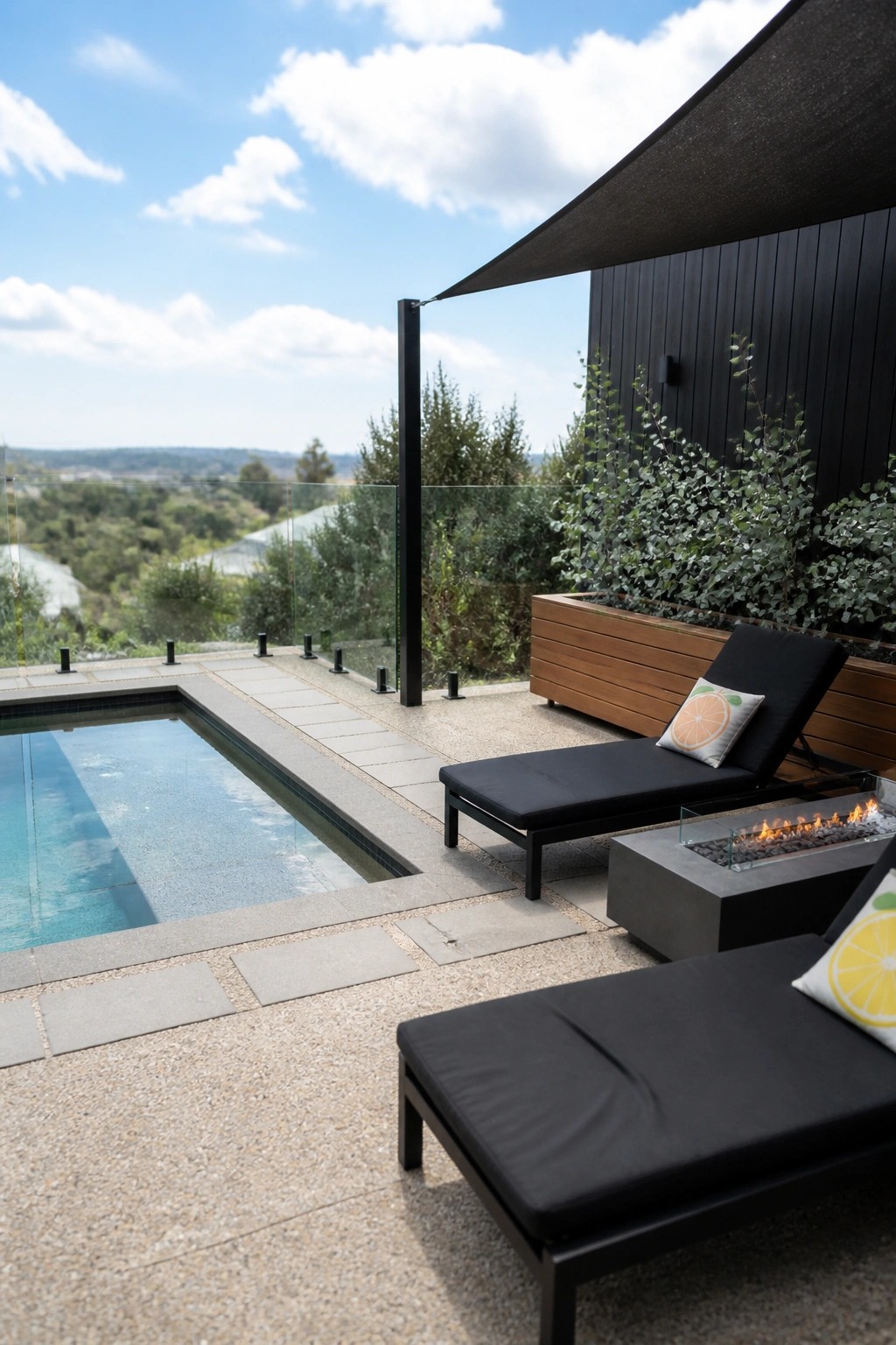 A small pool deck with two black lounge chairs, a concrete fire pit, and a dark shade sail stretched overhead above the seating area.