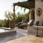 Wooden pergola with vines shades two striped lounge chairs on a stone patio beside a pool, with terracotta pots and a small side table.