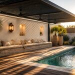 A covered poolside patio with a dark slatted roof, built-in bench seating with cushions along a white wall, potted palm plants, and a long rectangular pool with blue water.