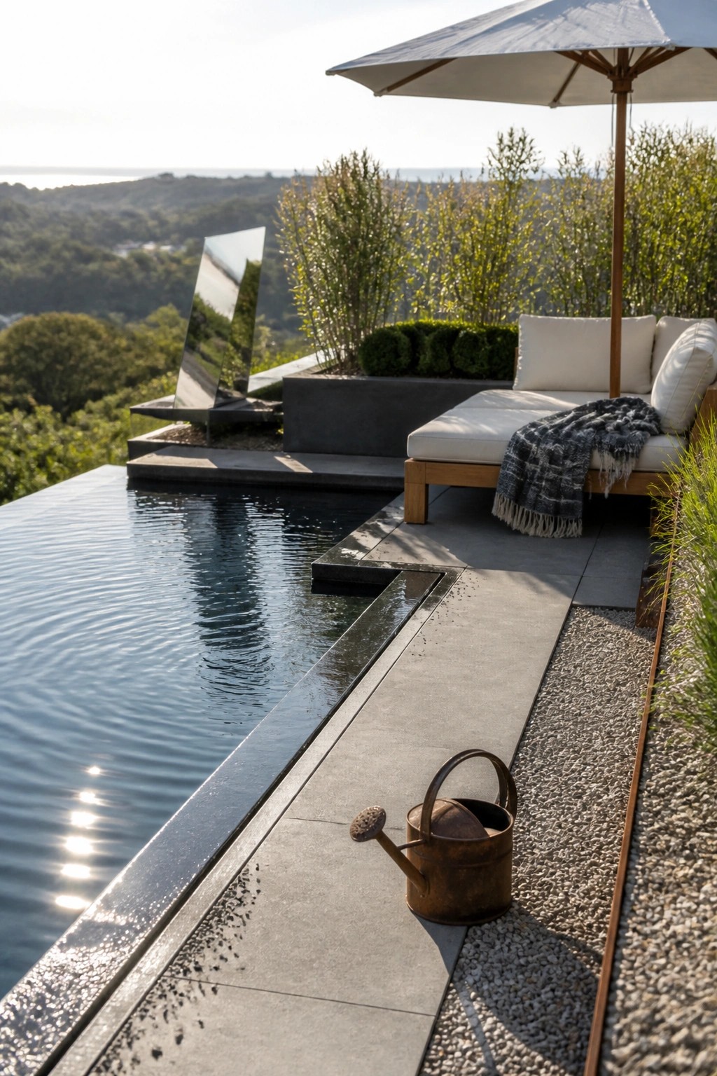 Infinity pool deck with lounge chair, umbrella, sculpture, and rusted watering can