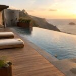 Infinity pool on cliff overlooking sea at sunset with lounge chairs and fire pit