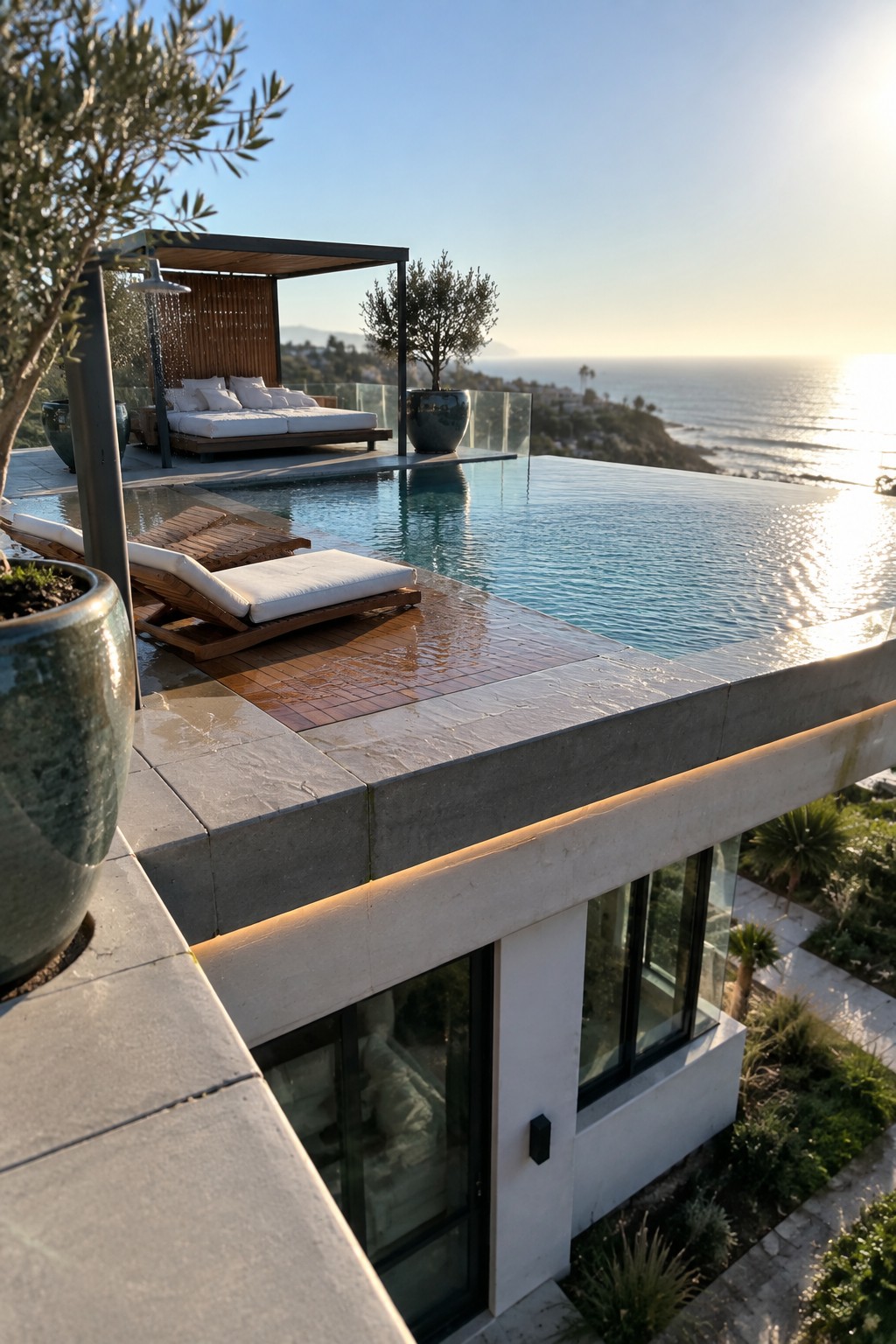 14 Elevated Infinity Pool Ideas Featuring Raised Architectural Structures A modern infinity pool sits on a raised concrete terrace with wooden lounge chairs, a canopy daybed, and an ocean view at sunset.
