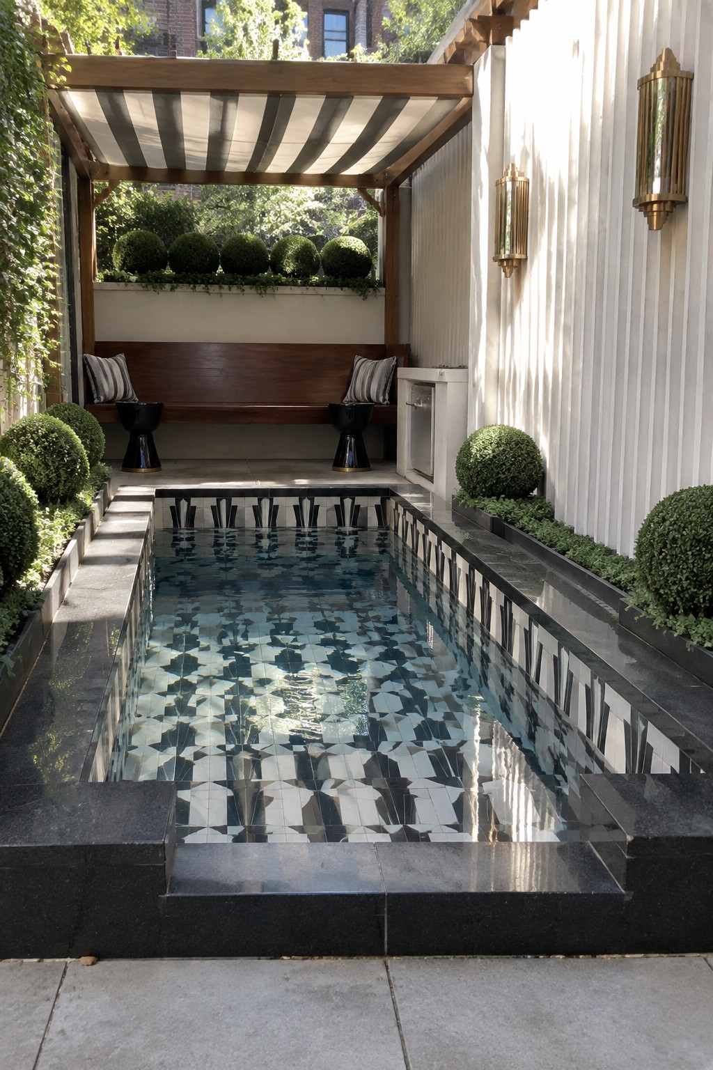 17 Bold Rectangular Plunge Pool Ideas for Narrow Outdoor Spaces A narrow rectangular plunge pool lined with black and white geometric tiles sits under a striped awning in a walled urban courtyard with built-in bench seating.
