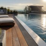 Luxury infinity pool with lounge chairs on wooden deck overlooking hills at sunset