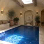 An indoor pool with blue mosaic tile, a stone fountain set in an arched niche at the far end, and built-in seating with cushions along one wall.
