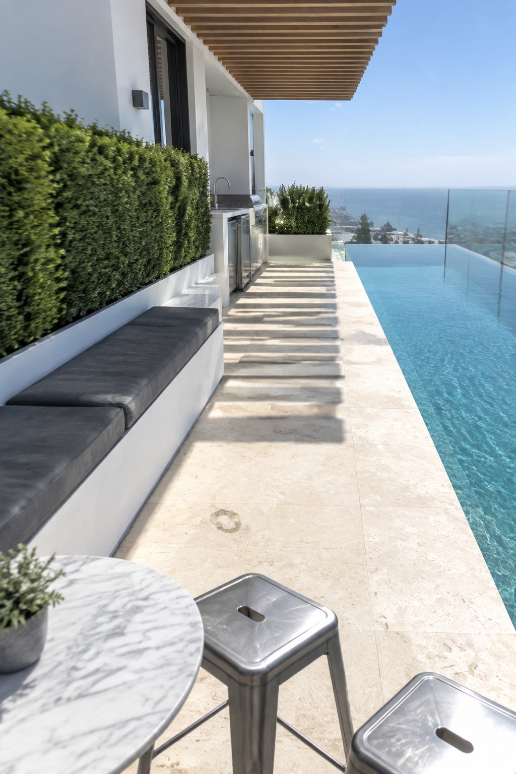 Modern luxury patio with infinity pool, ocean view, outdoor kitchen, and lounge seating.