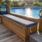 An above ground pool on a wooden deck with a blue striped cushioned storage bench, a locked stainless steel cabinet underneath, stacked labeled crates, and a gray step stool.