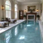 Luxurious indoor lap pool in marble hall with white columns and arched windows.