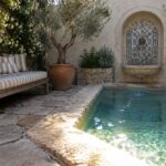 Rectangular turquoise pool with arched blue-tiled fountain, terracotta urn, and striped bench on stone patio