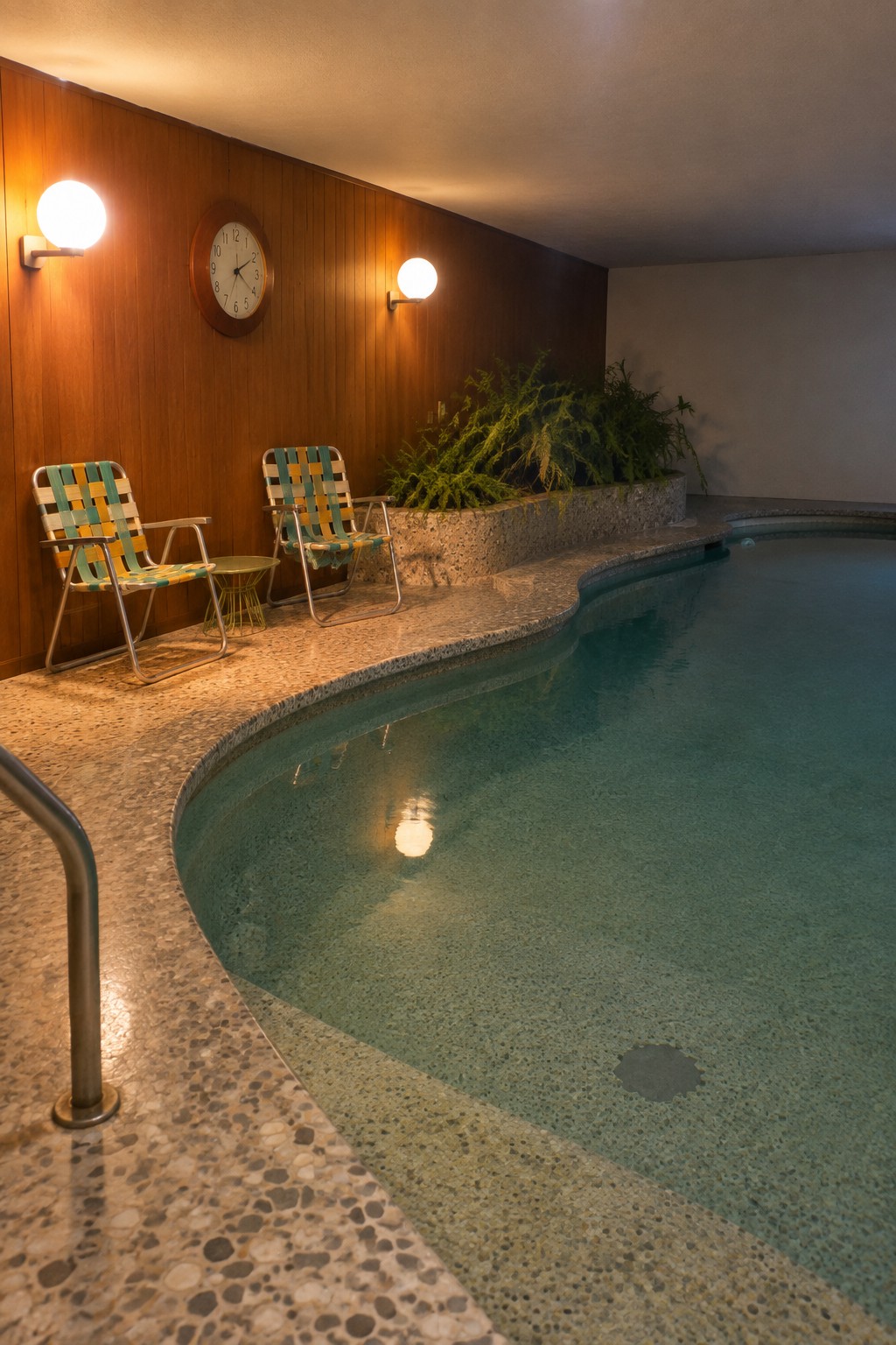 Retro indoor pool with two checkered lounge chairs on terrazzo deck.