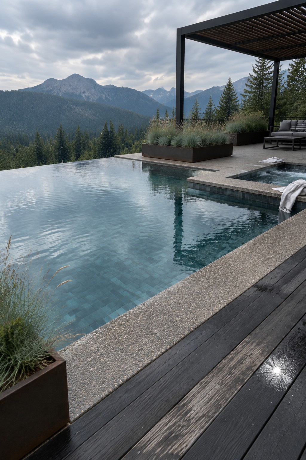 An infinity pool with blue-green glass mosaic tile, a dark wood deck, and mountain views in the background.
