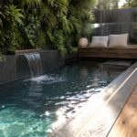 A rectangular plunge pool with dark tiles, a waterfall feature on one side, a wooden bench with cushions along the left edge, and linear LED lights along the deck borders.