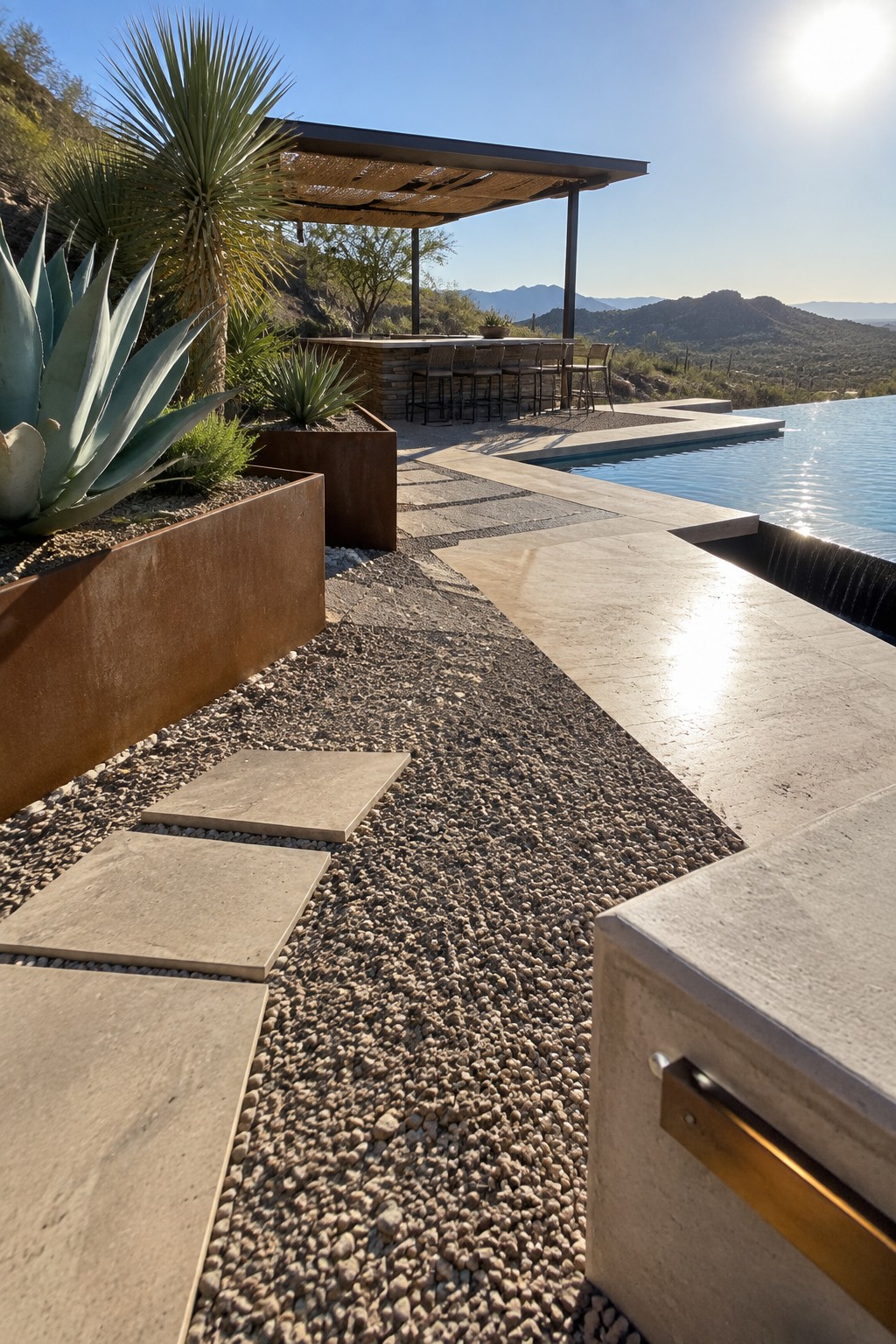 A hillside infinity pool with a covered outdoor bar and stools, stone decking, gravel paths, and large agave plants in rusted metal planters.