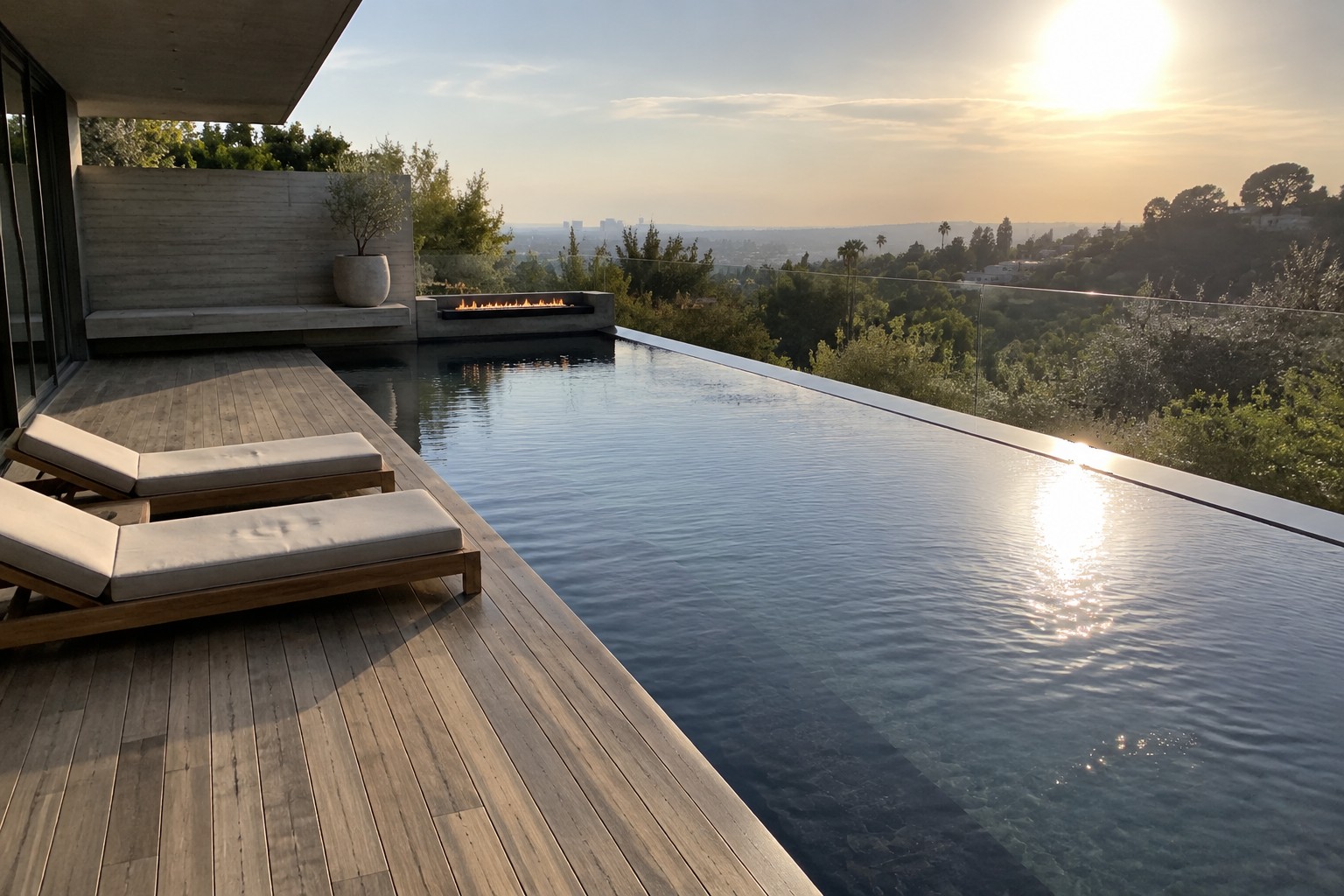 16 Sleek Modern Minimalist Infinity Pools With Restrained Architectural Details A long rectangular infinity pool with a glass edge sits next to a wide wooden deck holding two light-colored lounge chairs, with a built-in fire pit and distant city and water views in the background.