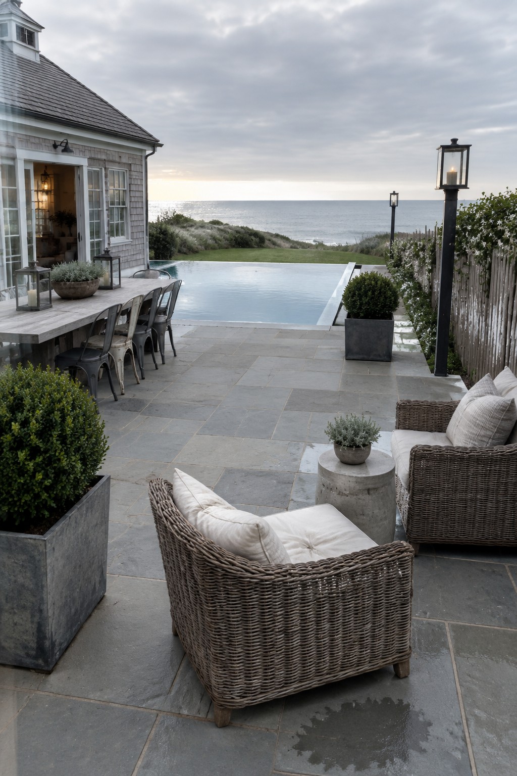 22 Breathtaking Ocean-View Infinity Pools Framed by Coastal Landscapes Stone patio with infinity pool, wicker chairs, dining table, and ocean view.