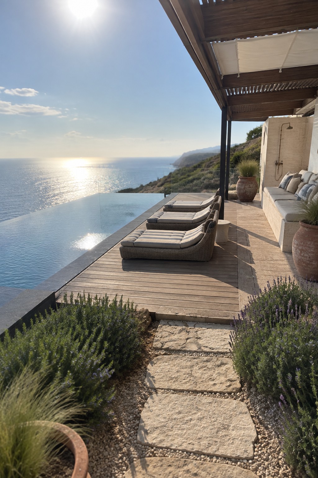 22 Breathtaking Ocean-View Infinity Pools Framed by Coastal Landscapes A wooden deck with four lounge chairs in a row beside an infinity pool overlooking the ocean, with stone steps and coastal plants nearby.