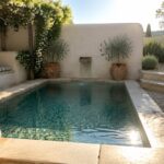 A small plunge pool with pebble bottom and natural stone surround, flanked by terracotta pots and lavender in a garden with a built-in bench and climbing vines.