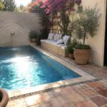 Narrow blue pool with fountain, pink bougainvillea, terracotta pots, and tiled patio