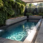 Modern courtyard pool with waterfall, fire pit, vertical garden, and lounge seating.